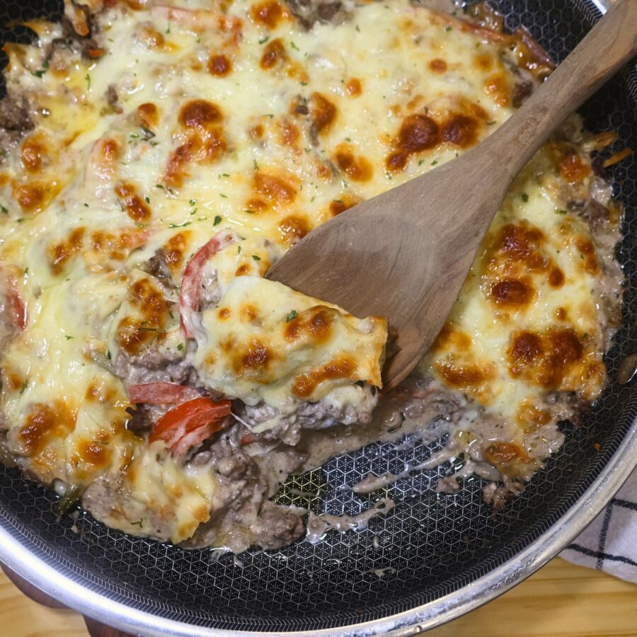 Ground Beef Cheesesteak Casserole in a skillet with a wooden spoon