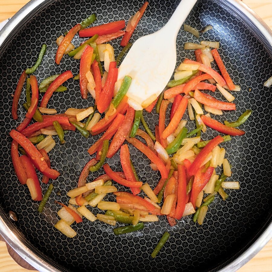 Overhead image of sliced peppers and onions in a skillet