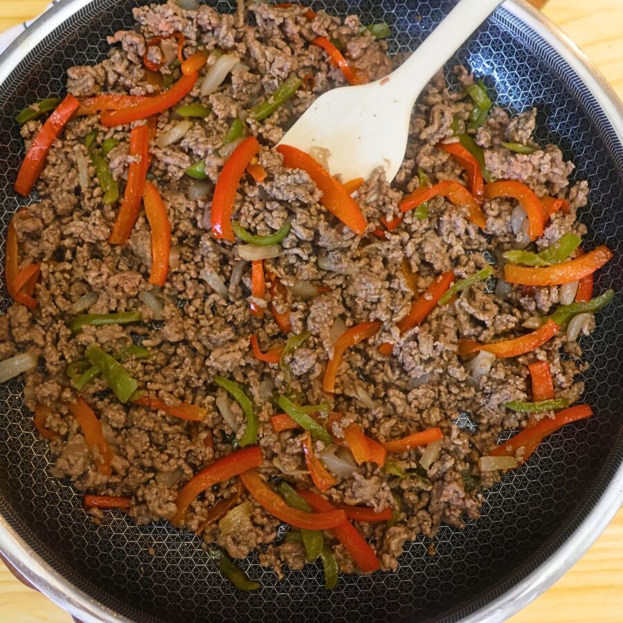 Cooked ground beef with peppers and onions in a skillet