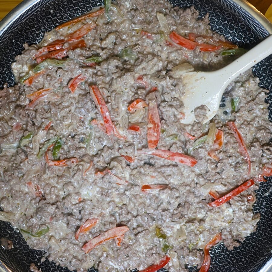 Seasoned and cooked ground beef in a skillet with peppers, onions, and cream cheese