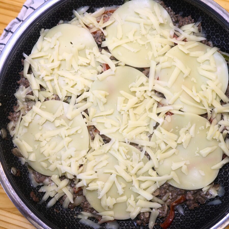 Overhead image of ground beef cheesesteak casserole covered in cheese before baking
