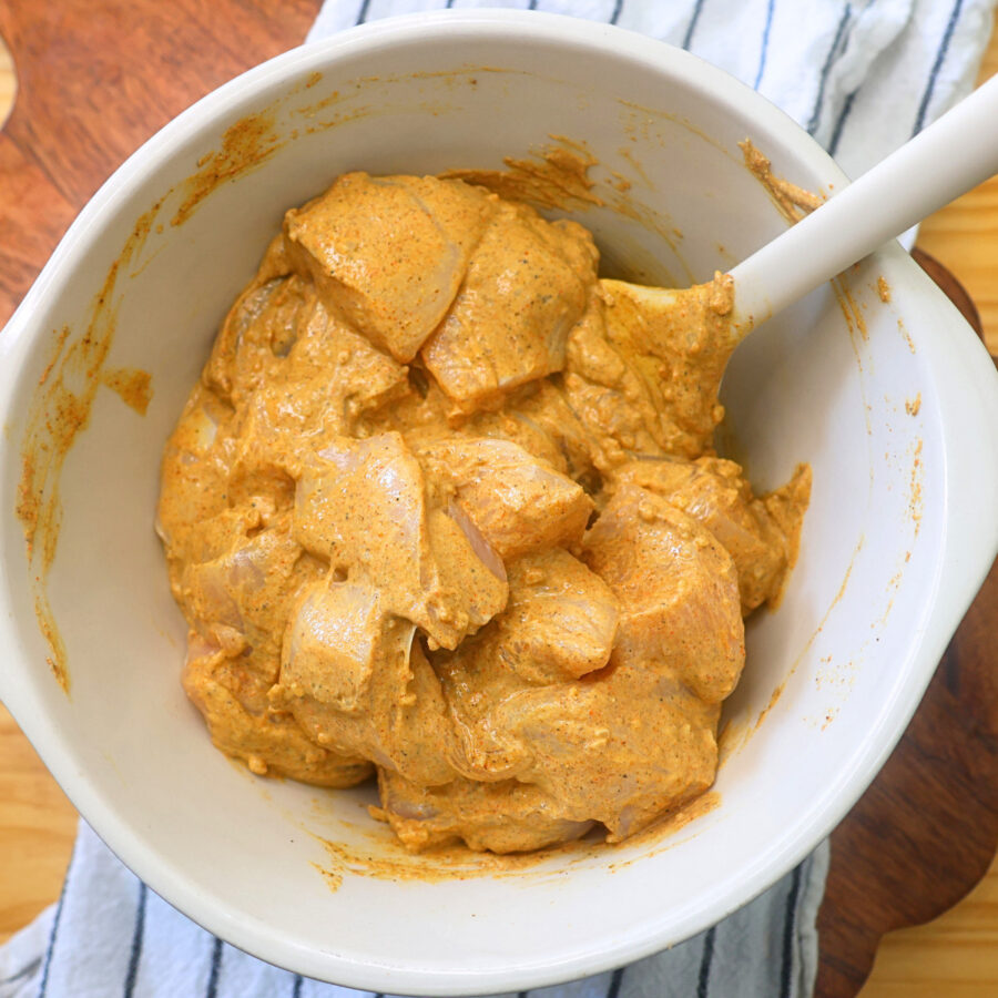 Chunks of uncooked chicken in a bowl with homemade spiced Greek yogurt marinade