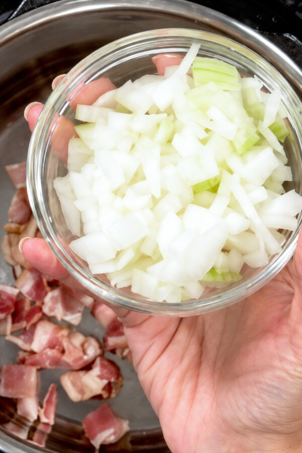 Diced onion being added to an Instant Pot with diced uncooked bacon