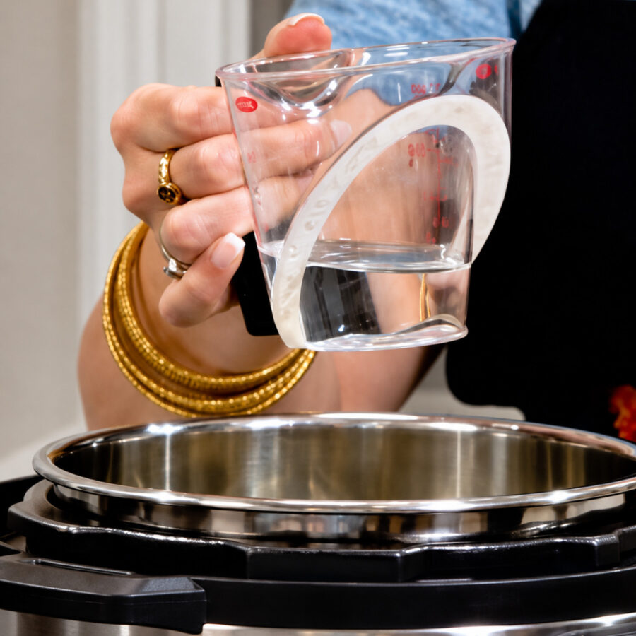 Water being added to an Instant Pot with green beans, bacon, and onion inside