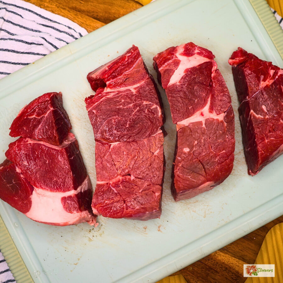 A chuck roast cut into 4 pieces on a cutting board