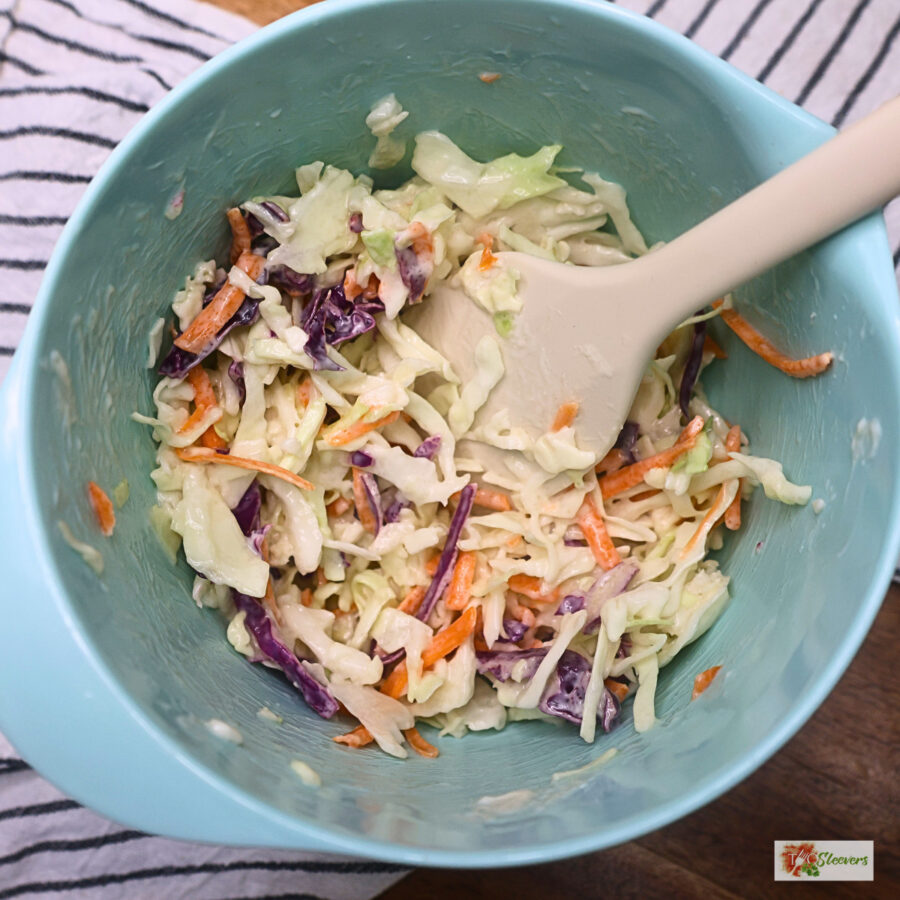 Homemade slaw in a blue bowl with a silicone spatula
