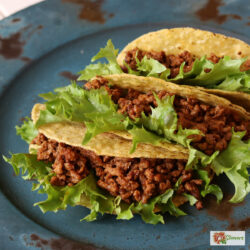 Three crunchy tacos with Instant Pot Taco Meat and lettuce on a blue plate