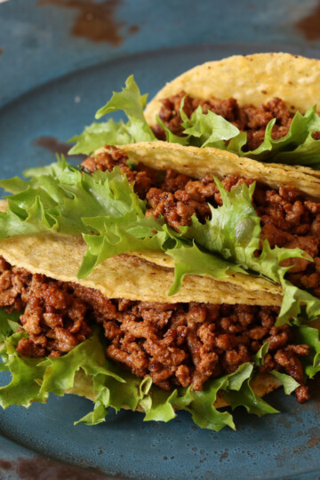Three crunchy tacos with Instant Pot Taco Meat and lettuce on a blue plate
