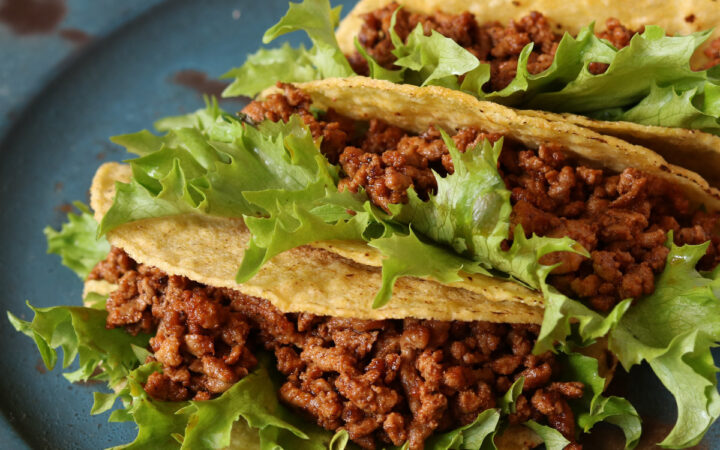 Three crunchy tacos with Instant Pot Taco Meat and lettuce on a blue plate