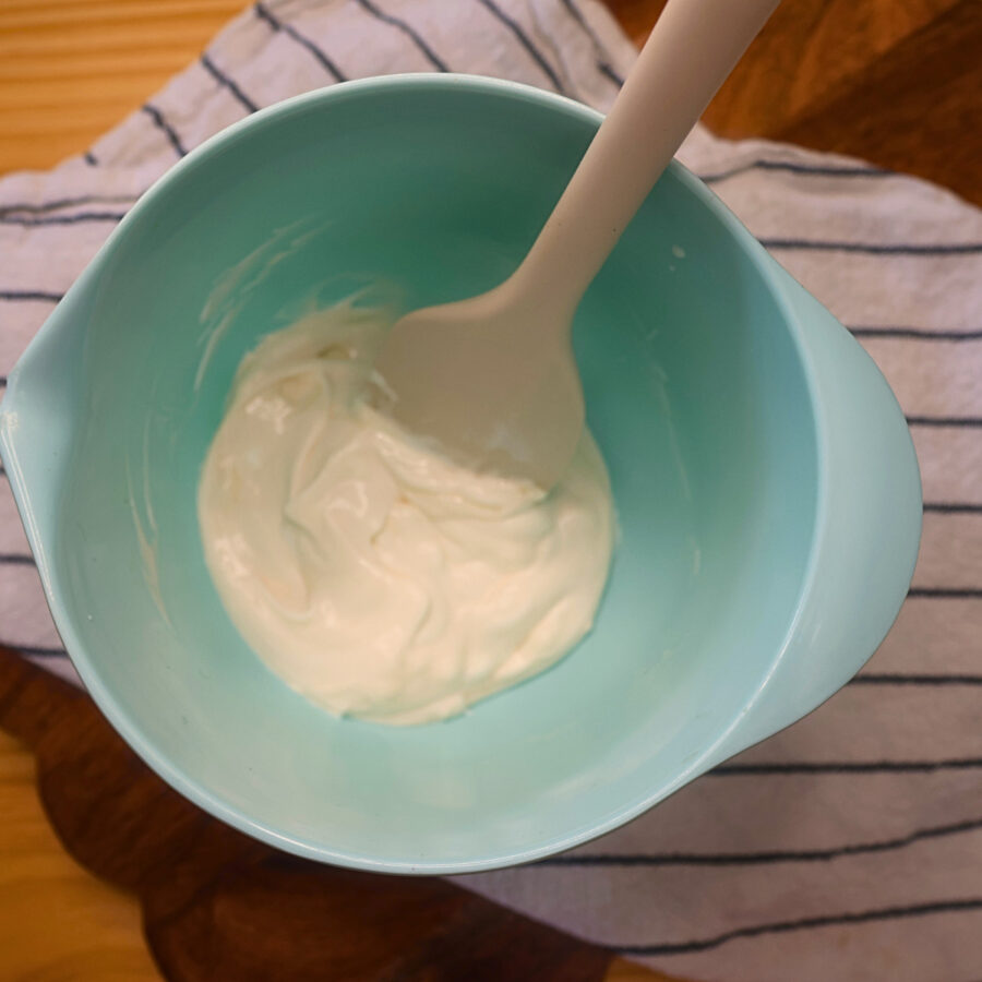 Homemade salad dressing for keto broccoli salad in a blue mixing bowl with silicone spatula