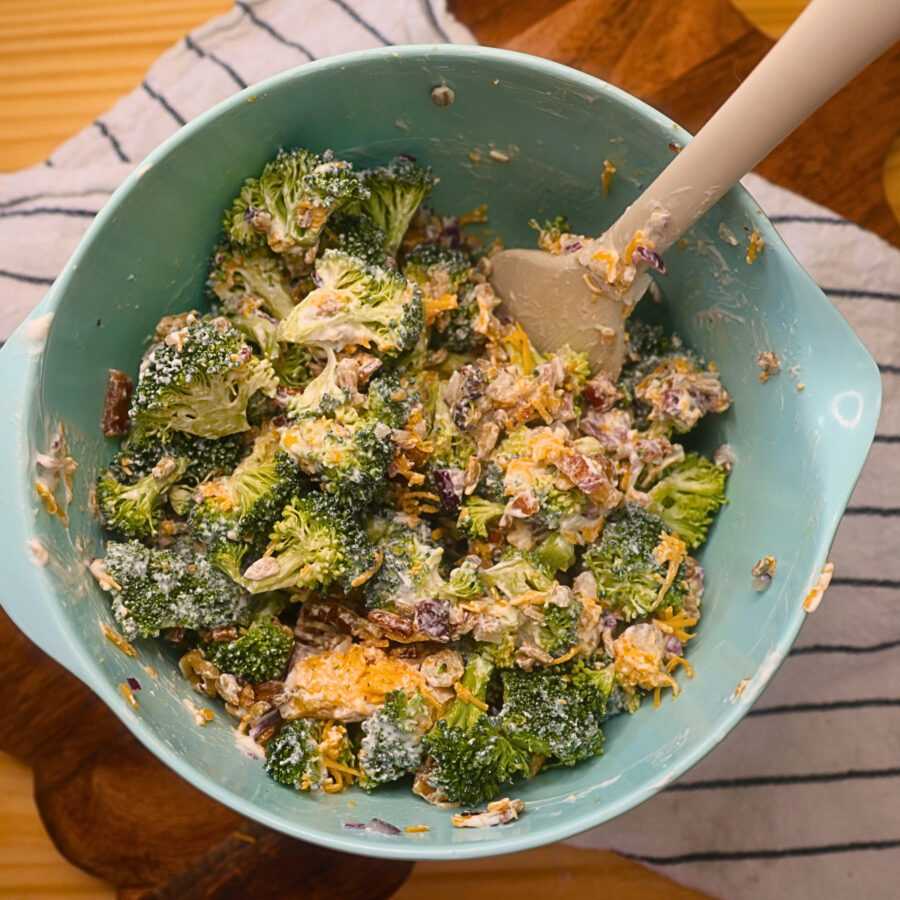 Assembled keto broccoli salad in a blue bowl with a silicon spatula