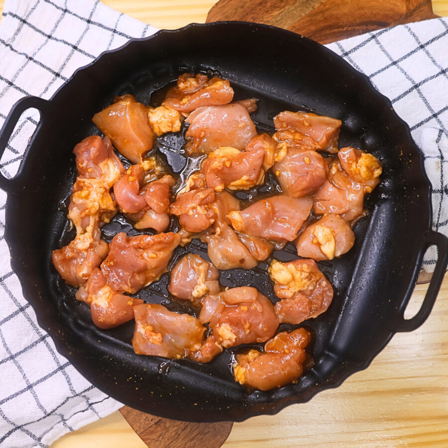 Uncooked marinated chicken thighs in an air fryer basket