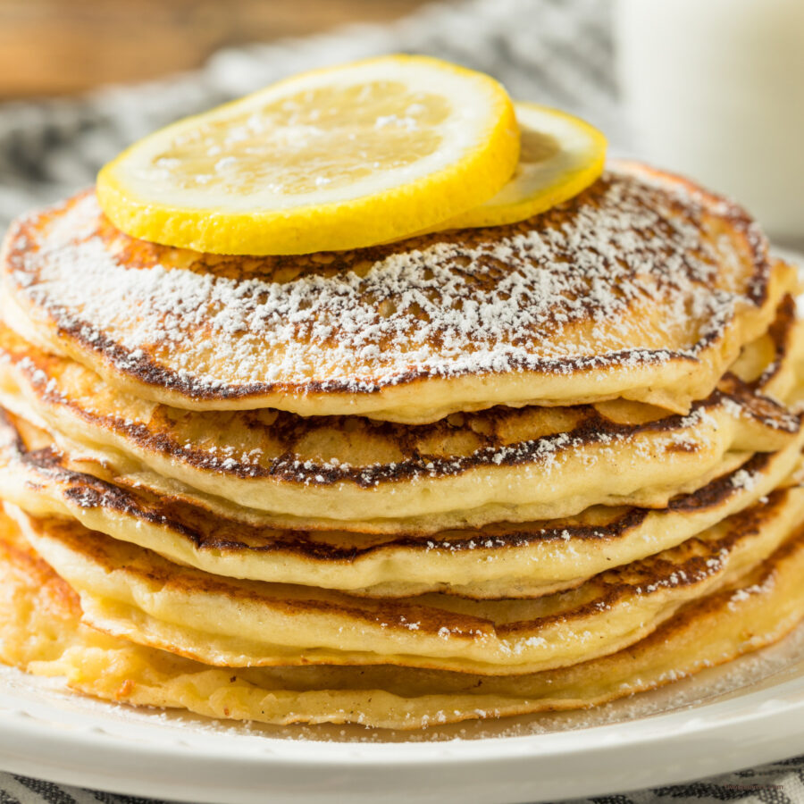 Close up image of a stack of lemon ricotta pancakes with sliced lemon on top