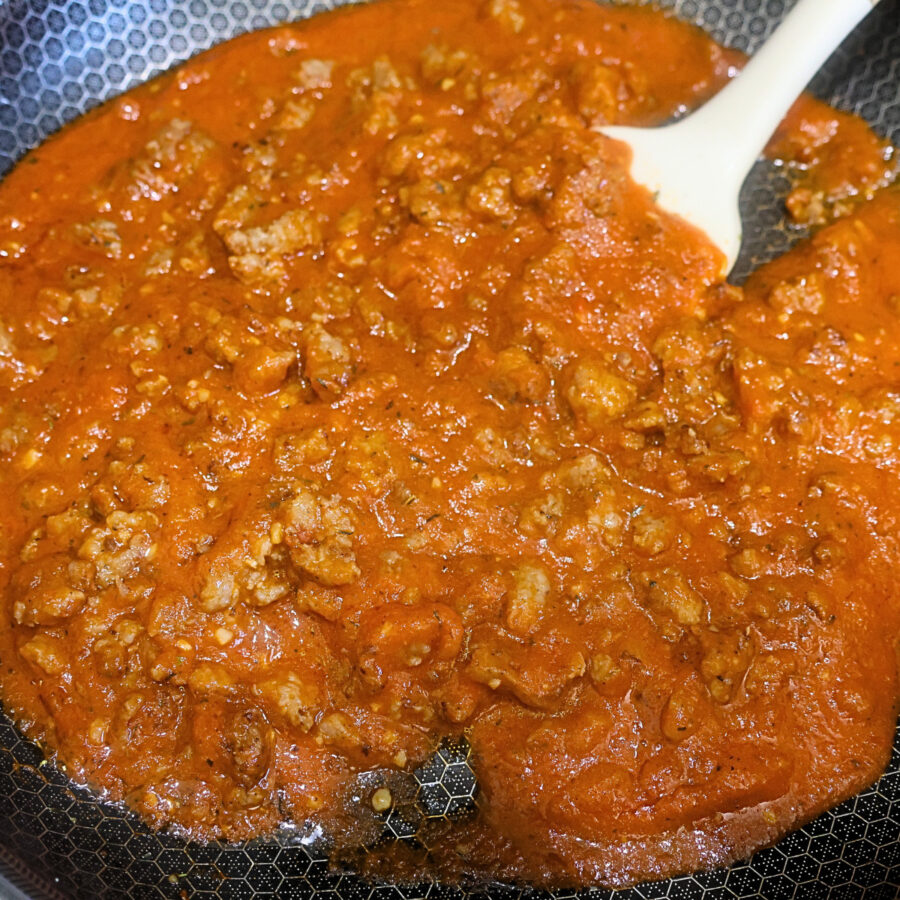 Ground sausage cooked with marinara sauce in a skillet with a spatula