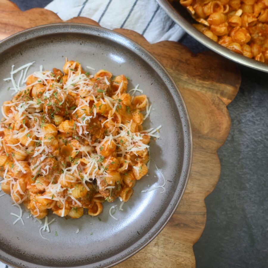 Mini meatball pasta on a plate with the pan of it side by side