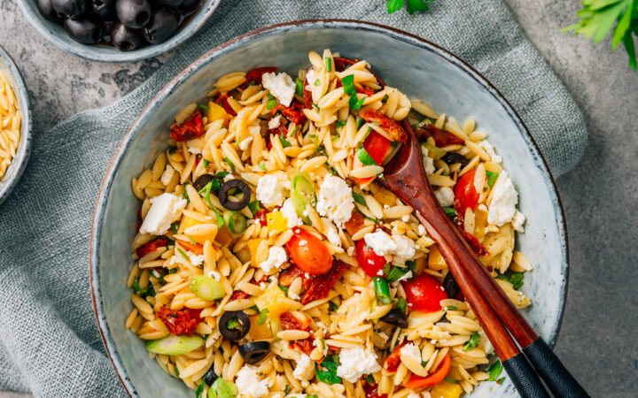 Overhead image of Orzo Salad in a bowl with serving spoons