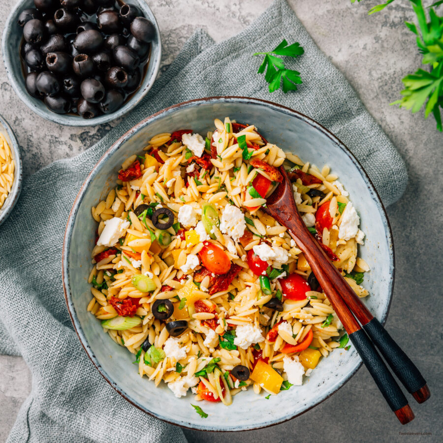 Overhead image of Orzo Salad in a bowl with serving spoons