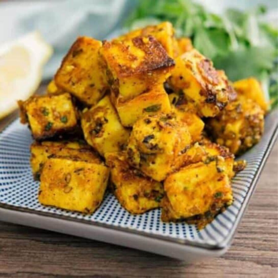 Paneer Tikka piled on a plate with lemon and cilantro