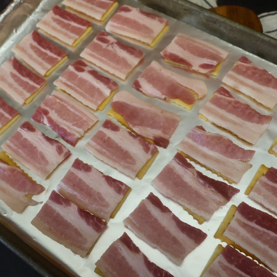 Raw pieces of bacon on top of crackers on a baking sheet