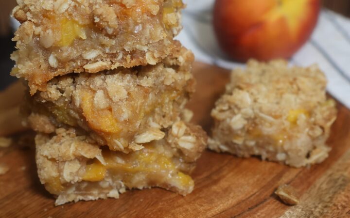 Close up image of peach Crumble Bars stacked on a wooden serving board