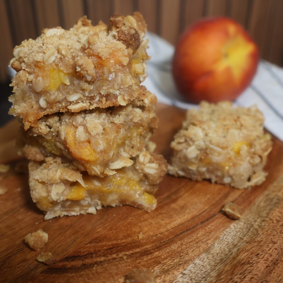 Close up image of peach Crumble Bars stacked on a wooden serving board