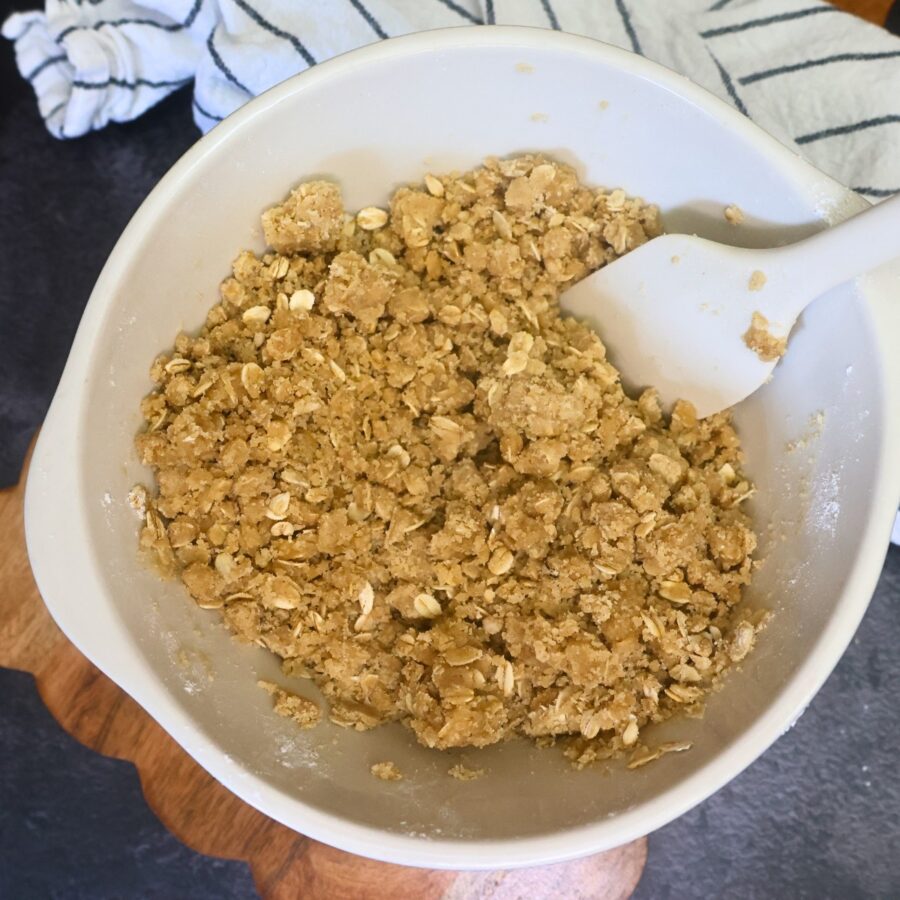 Crust and crumble topping for peach crumble bars in bowl with a silicone spatula