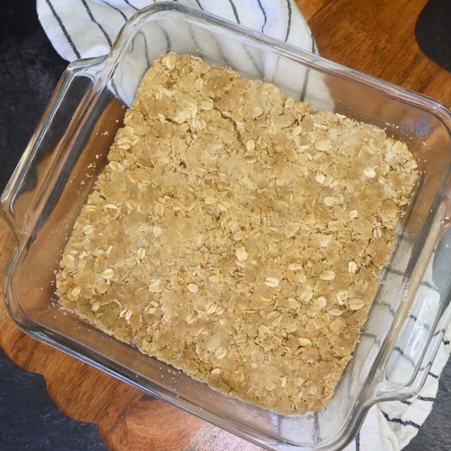 Crust for peach crumble bars pressed into a glass baking dish