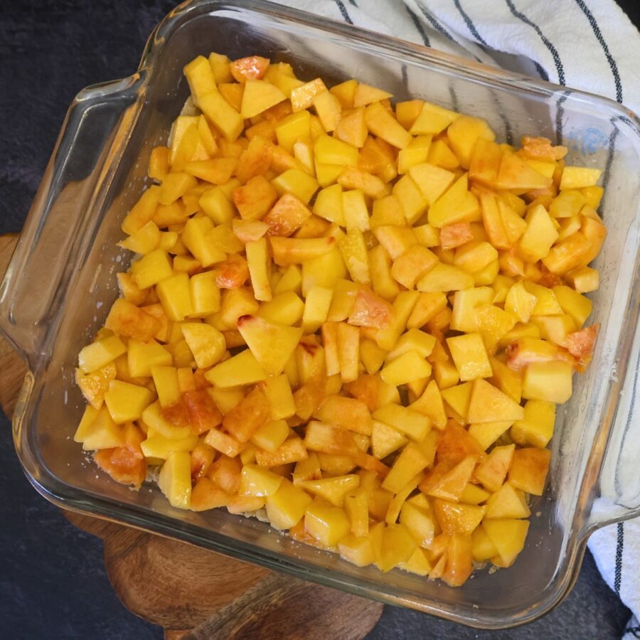 Peach filling over the peach crumble bar crust in a glass baking dish