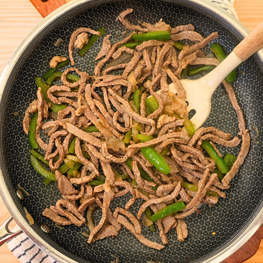 Cooked thin sliced steak with onions and peppers in a skillet