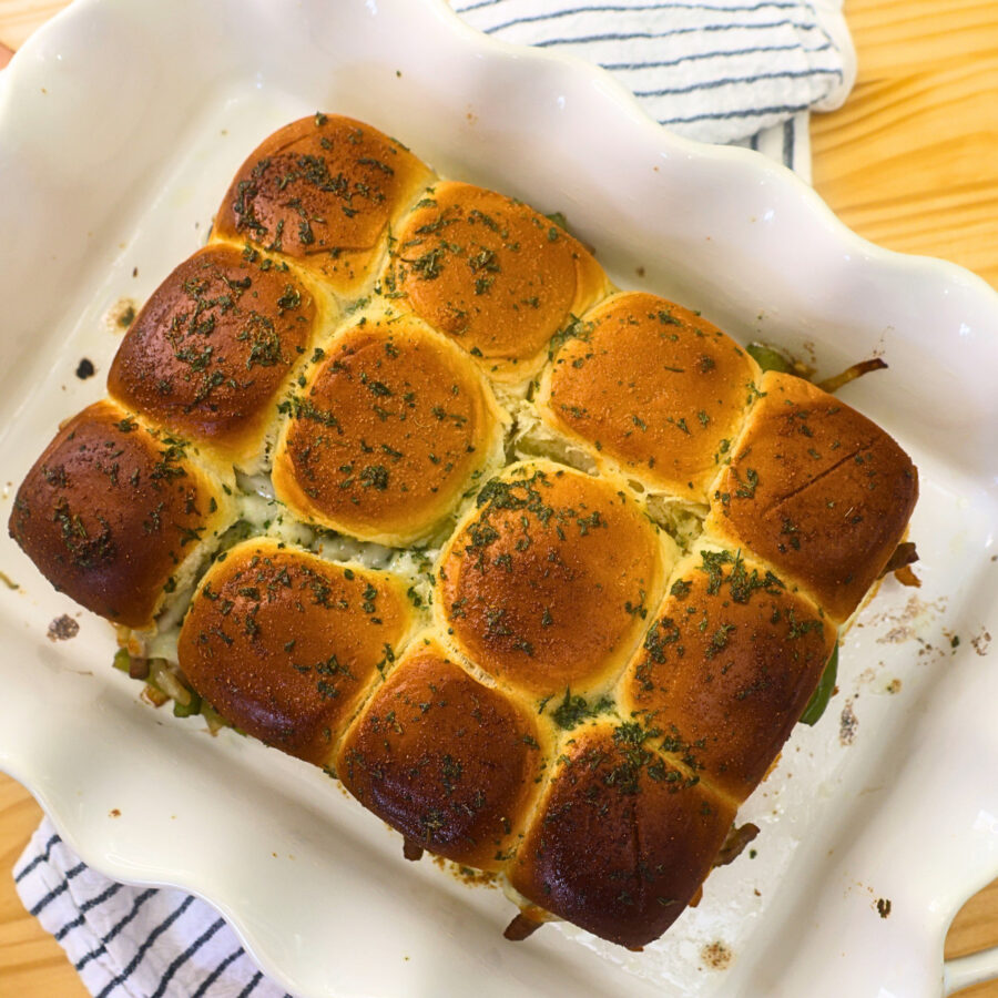 Overhead image of 12 baked cheesesteak sliders in a pan