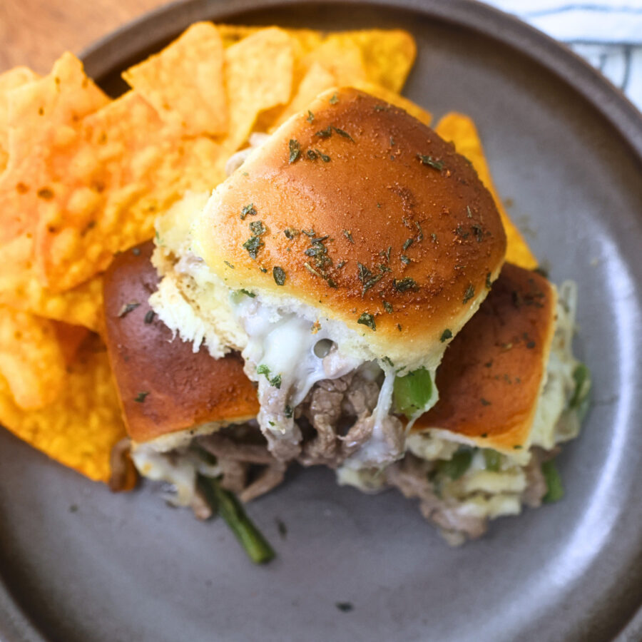Three Philly Cheesesteak sliders stacked on top of each other on a plate with chips