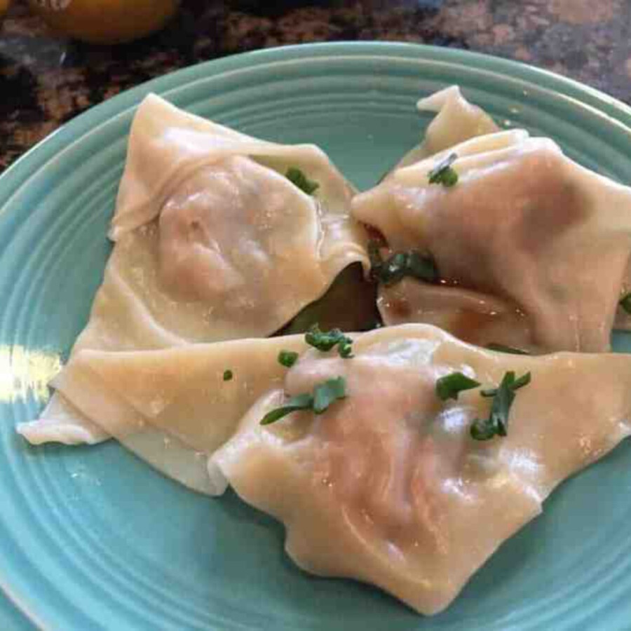three cooked homemade pork wontons on a blue plate