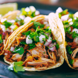 Three shredded beef tacos on a plate with veggie garnish