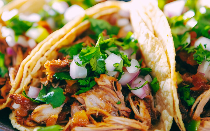 Three shredded beef tacos on a plate with veggie garnish