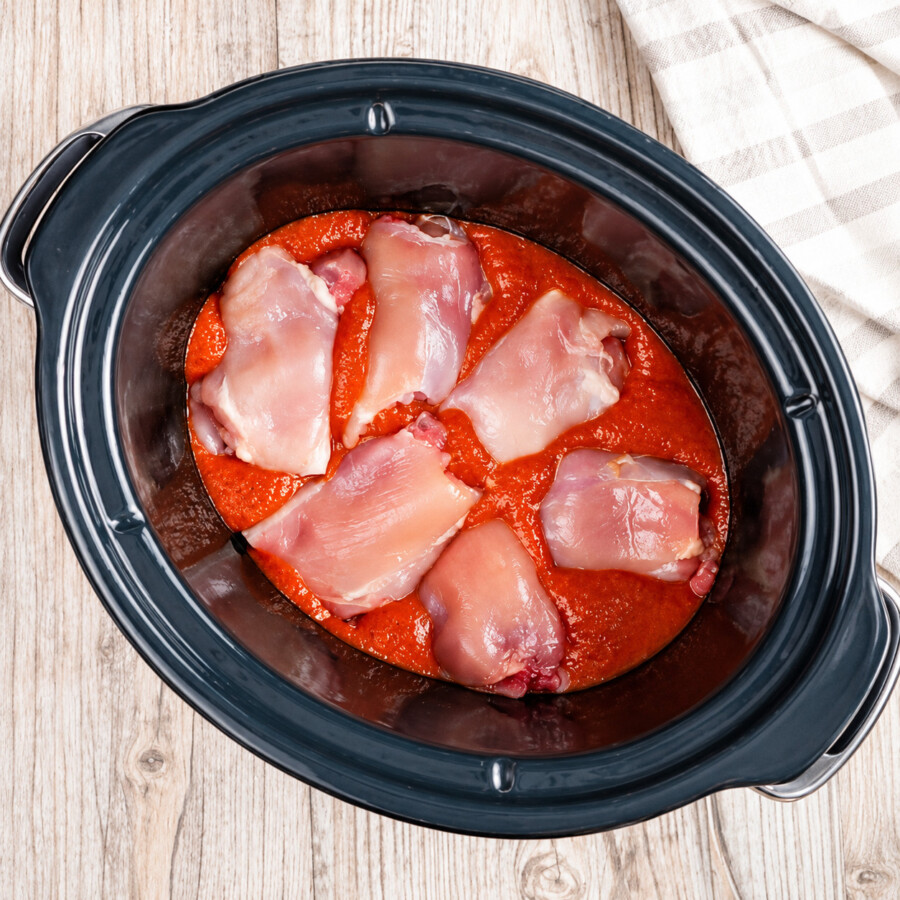 Uncooked chicken thighs on top of blended sauce in a slow cooker