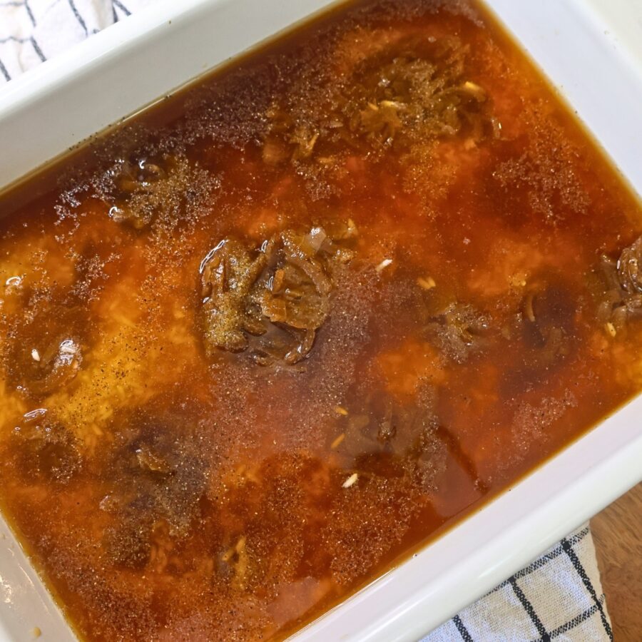A baking dish with rice, soup, broth, and seasoning in it