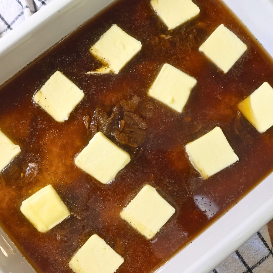 A baking dish with rice, soup, broth, and seasonings topped with pats of butter