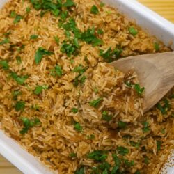 Stick of butter rice in a baking dish being served with a wooden spoon