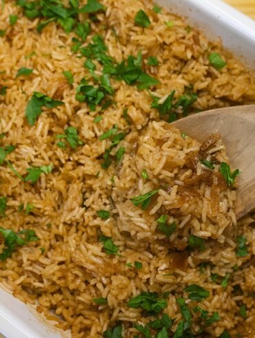 Stick of butter rice in a baking dish being served with a wooden spoon