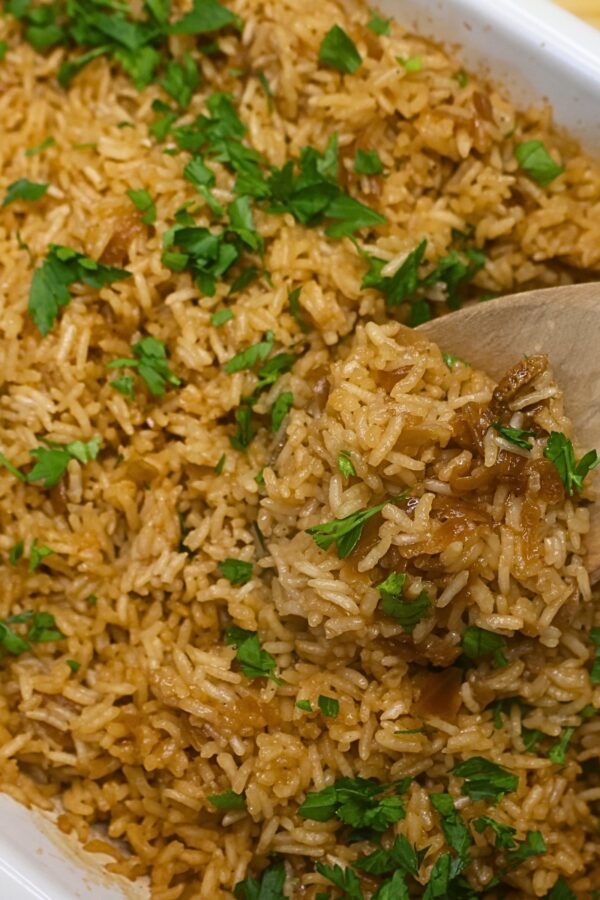 Stick of butter rice in a baking dish being served with a wooden spoon
