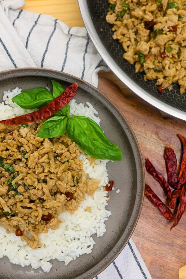 A plate of Thai Basil Chicken over rice with a skillet for serving next to it