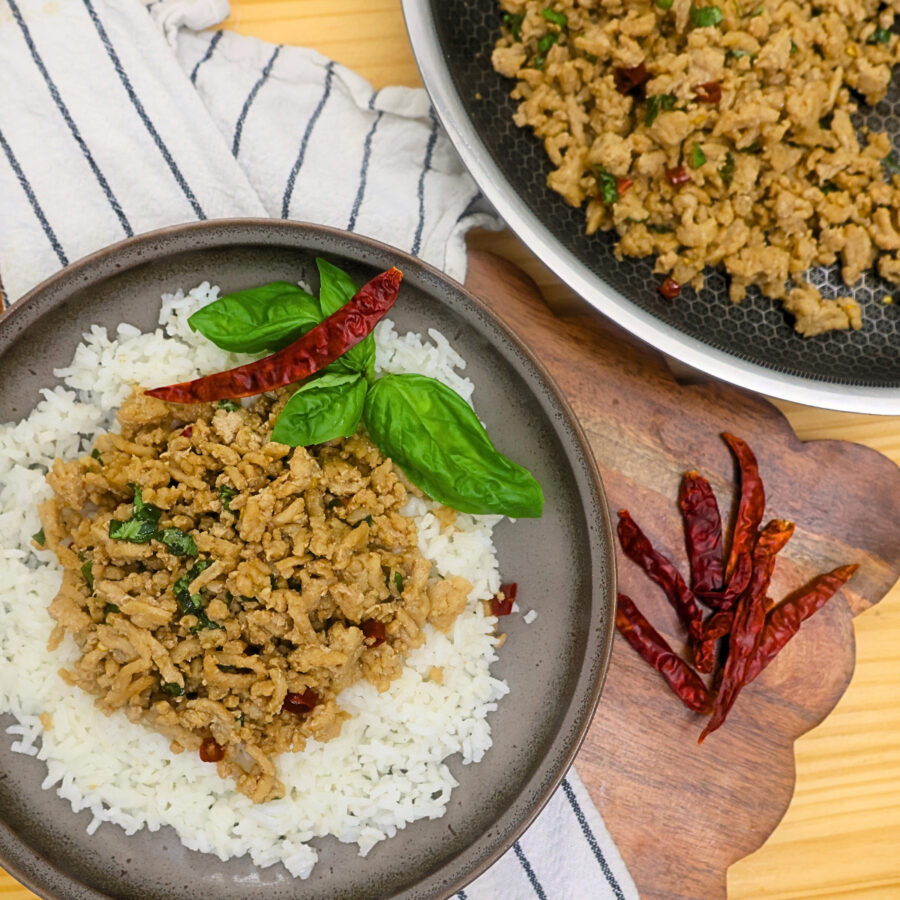 A plate of Thai Basil Chicken over rice with a skillet for serving next to it