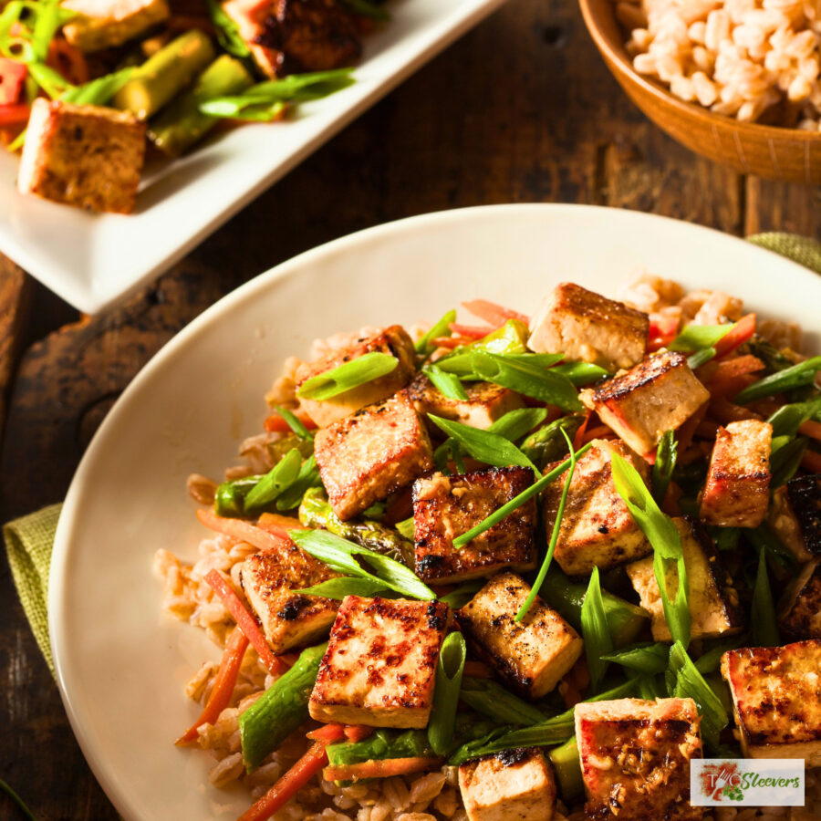Tofu stir fry on a plate over rice with a serving dish of it next to the plate