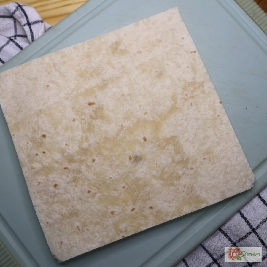 A stack of flour tortillas cut into squares on a cutting board