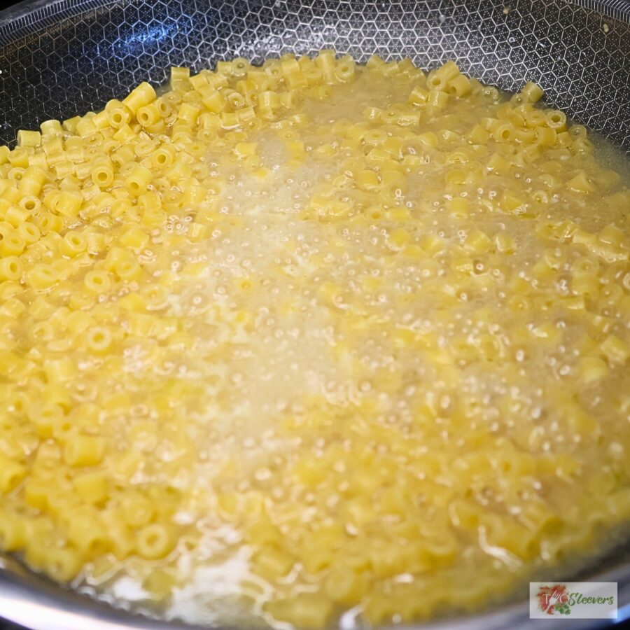 Ditalini pasta cooking in a skillet of chicken broth