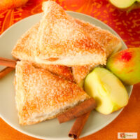 Overhead image of Apple Turnovers on a plate with cinnamon sticks and sliced apple