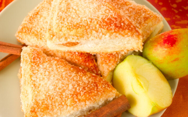 Overhead image of Apple Turnovers on a plate with cinnamon sticks and sliced apple