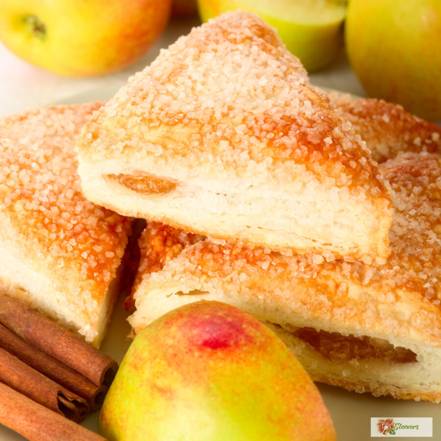 Close up image of apple turnovers stacked on a plate with apples and cinnamon sticks