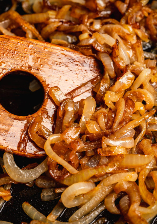 Close up image of caramelized onions being stirred with a wooden spatula