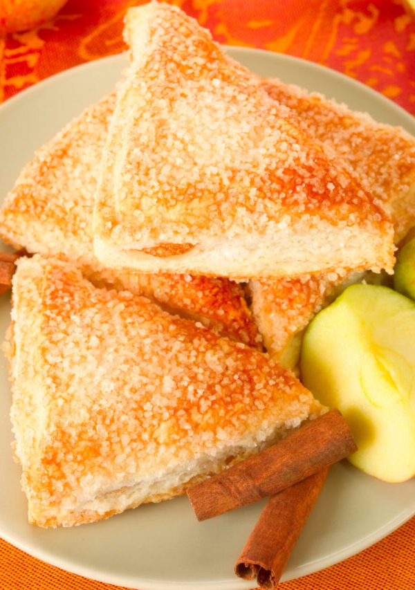 Overhead image of Apple Turnovers on a plate with cinnamon sticks and sliced apple